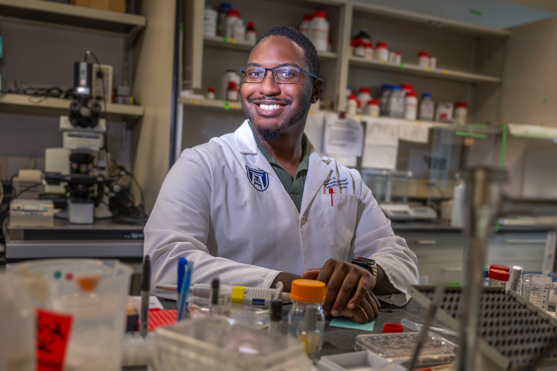 A male scientist sits at a table in a scientific lab.