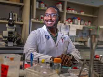 A male scientist sits at a table in a scientific lab.