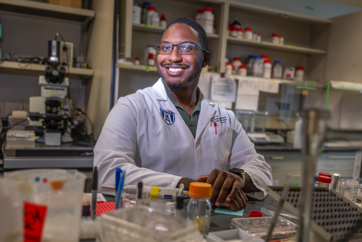 A male scientist sits at a table in a scientific lab.