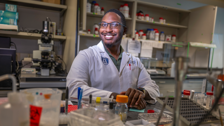 A male scientist sits at a table in a scientific lab.