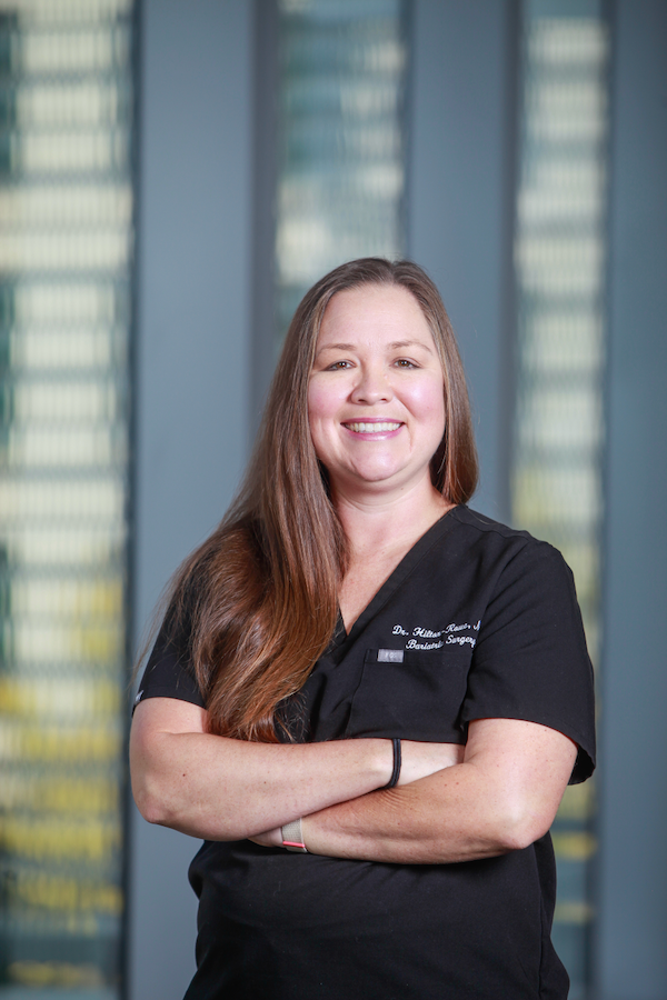 A female doctor in medical scrubs stands in the hallway of a hospital.
