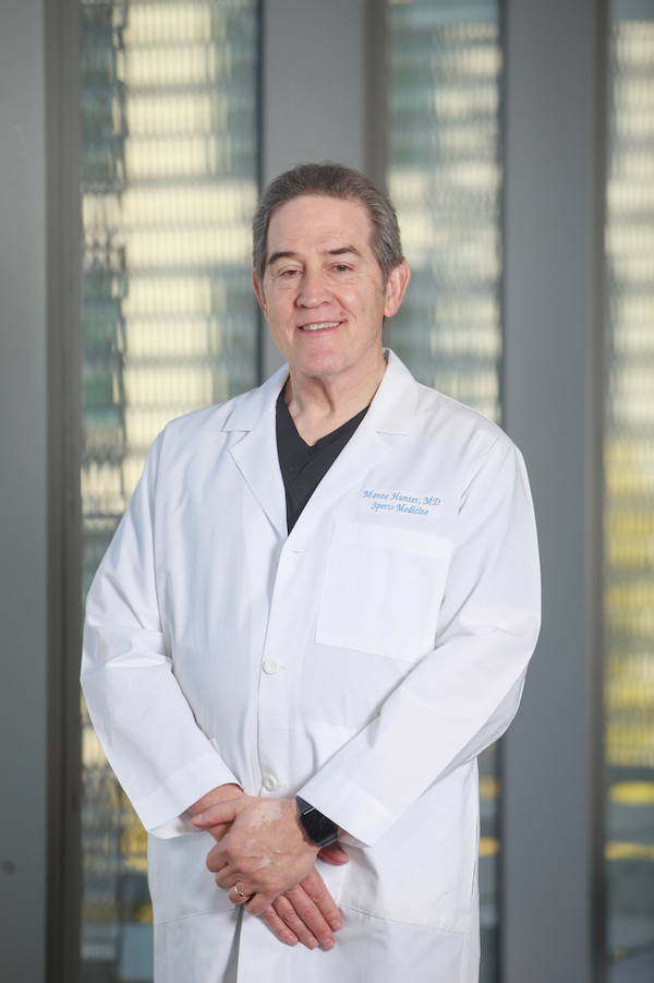 A male doctor in his lab coat stands in the hallway of a hospital.