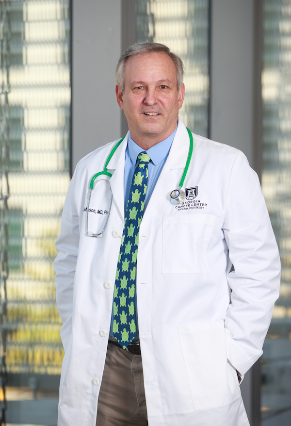 A male doctor in his lab coat stands in the hallway of a hospital.