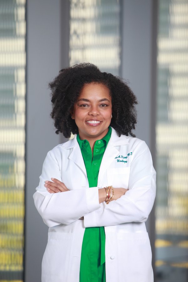 A female doctor in her lab coat stands in the hallway of a hospital.