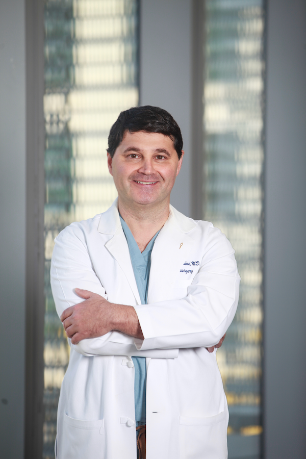 A male doctor in his lab coat stands in the hallway of a hospital.