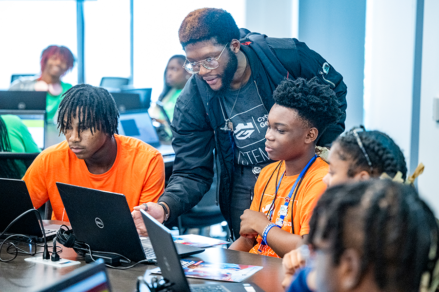 A college man helps two high school students during a competition on laptop computers.
