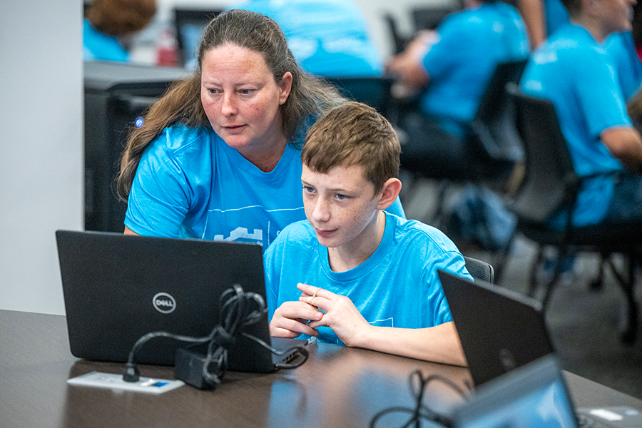 A woman helps a high school boy with a computer problem.