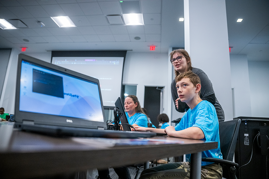 A college woman and a high school boy look at an overhead projector screen for instructions during a competition.
