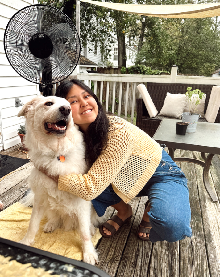 A college-aged woman hugs a dog on a porch.