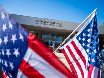 The exterior of a large theatre in the background with American flags in the foreground.