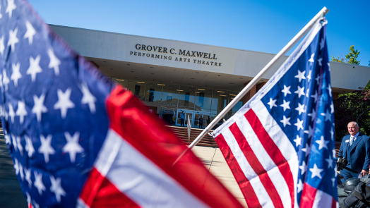 The exterior of a large theatre in the background with American flags in the foreground.