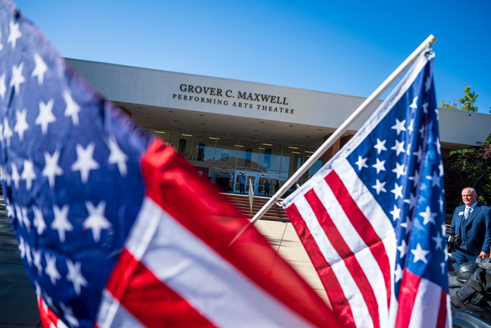 The exterior of a large theatre in the background with American flags in the foreground.