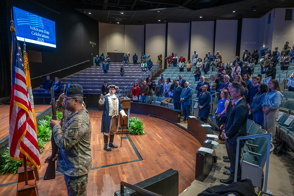 A man in period dress speaks in a theater filled with people.