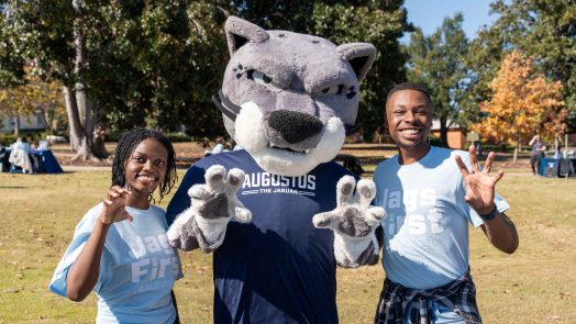 Augusta University's jaguar mascot, Augustus, and two students hold their hands like a paw.