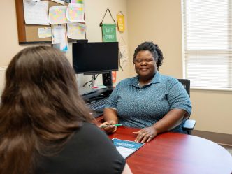A woman smiles at a young student across from a desk.