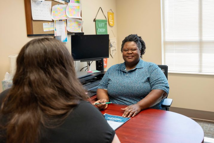 A woman smiles at a young student across from a desk.