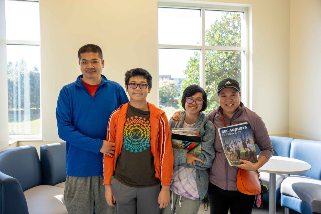 A family of four, including one high school aged boy, a high school aged girl, and a mom and dad, all taking a tour on a college campus.