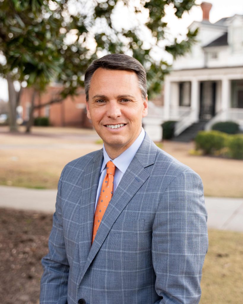 A man stands outside smiling with a building in the background.