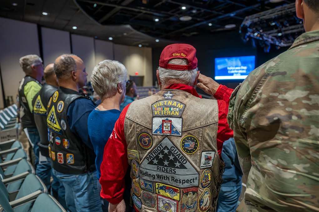The backs of several men and a woman dressed in clothing with patriotic decor.