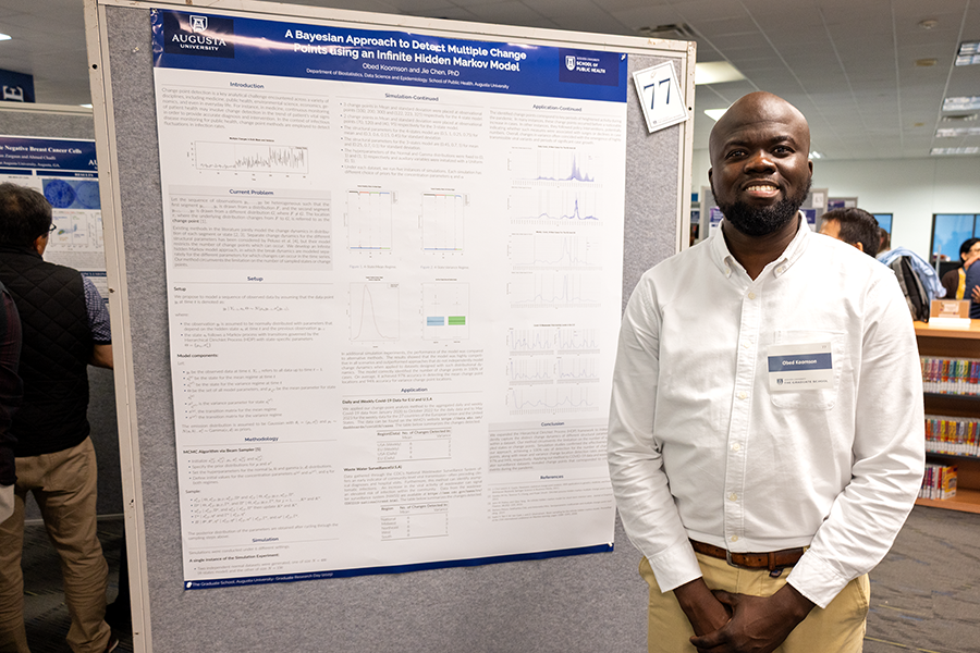 A male college student stands next to a scientific poster during a large poster presentation session.