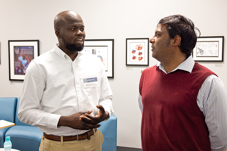 Two men stand next to a scientific poster and talk about the research that went into it.