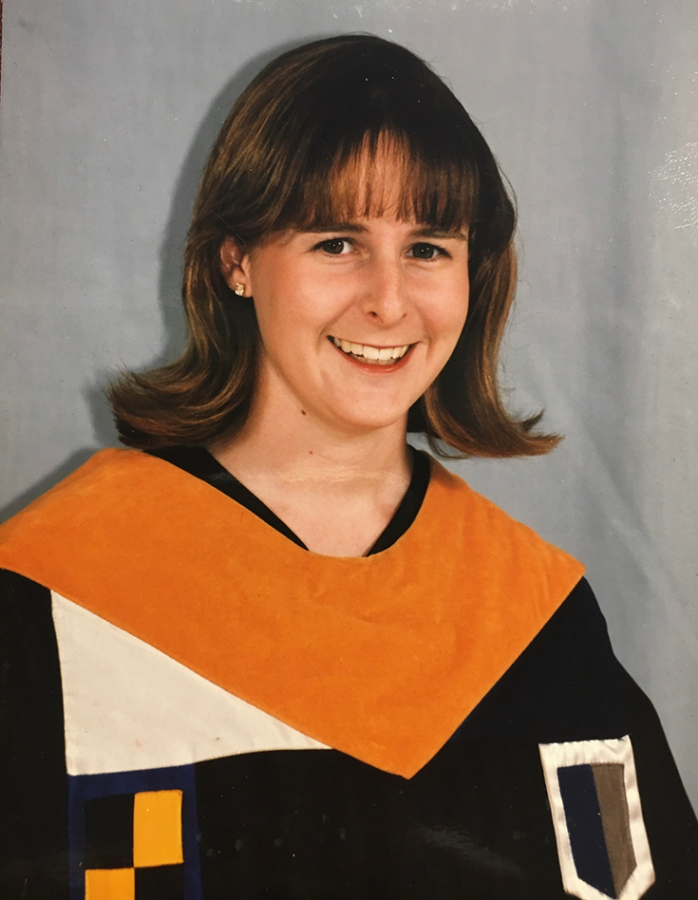 A woman poses for a picture wearing a graduation robe and stole.