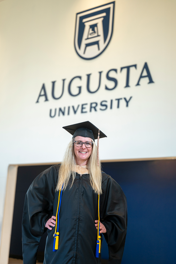 A woman wearing a graduation cap and gown stands with her hands on her hips.