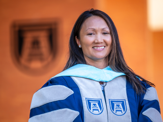 A woman wearing graduation regalia smiles at the camera.