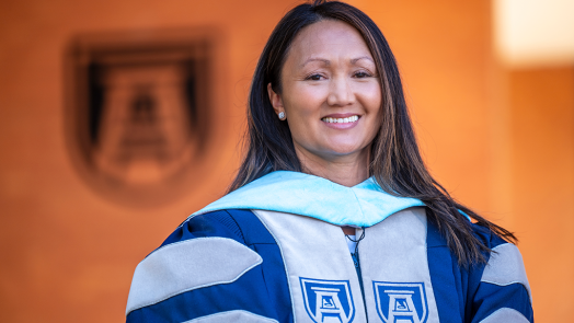 A woman wearing graduation regalia smiles at the camera.