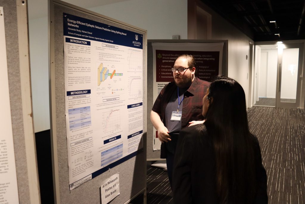 A male college student presents a scientific poster to a woman during a poster session.