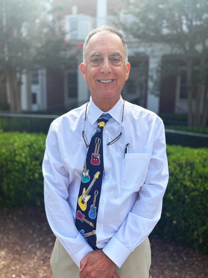 A male psychiatrist wearing a tie with guitars on it stands outside and smiles at the camera.