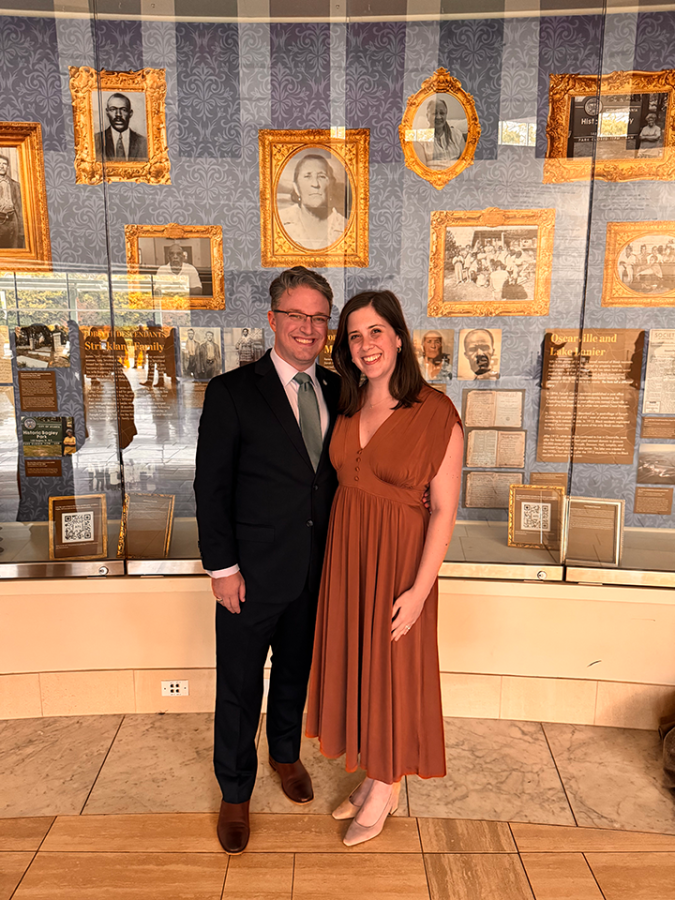 Man and woman smile in front of display of old photographs behind glass.