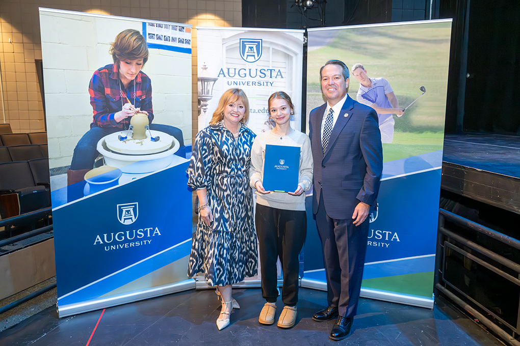 A university president and first lady pose with a high school student.