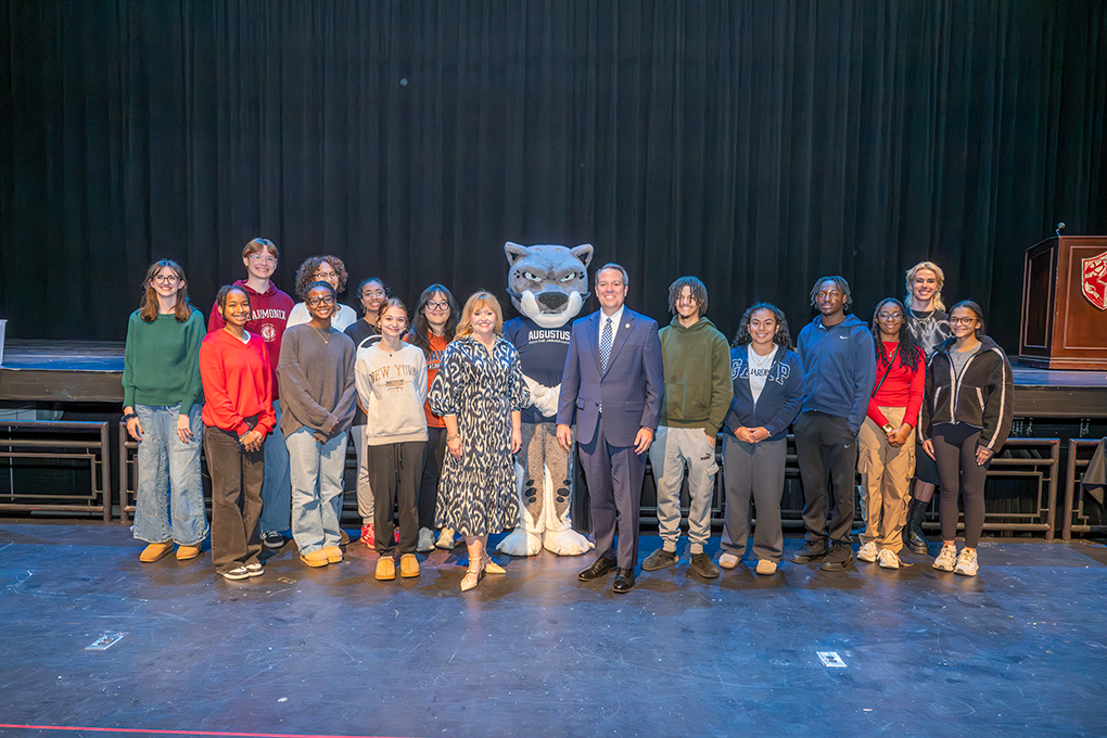 A president and first lady of a university posing with a group of high school students who were admitted to the university. In the middle stands the university mascot, a Jaguar.