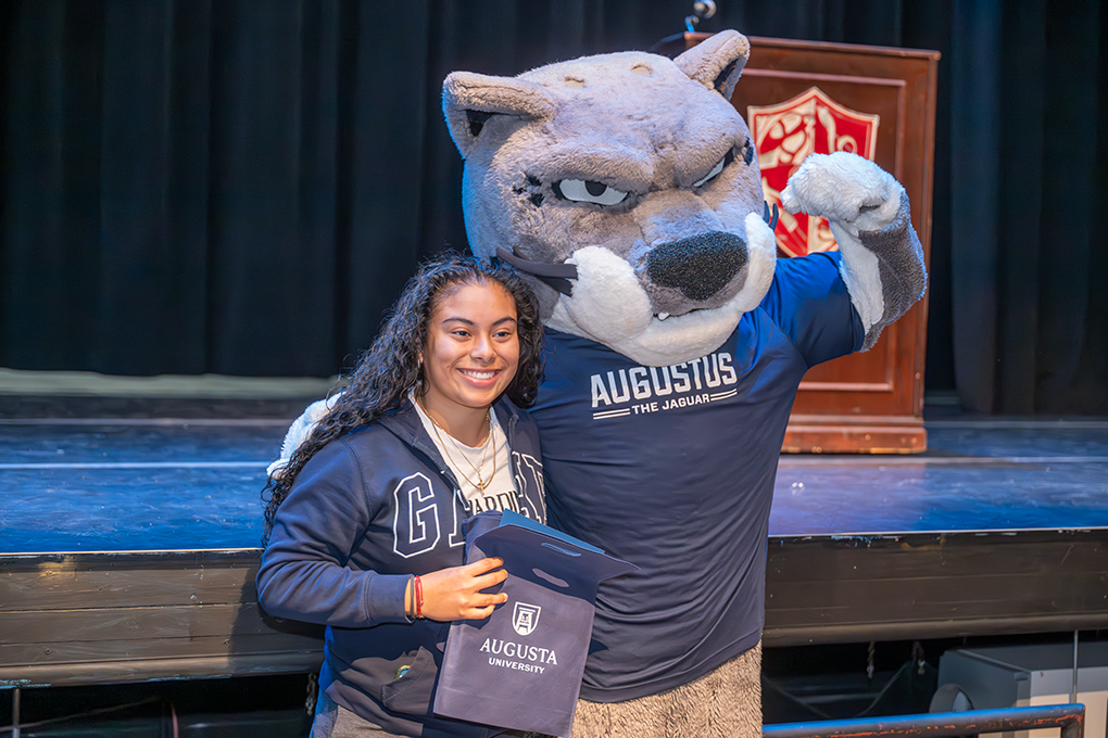 A high school girl poses with a Jaguar university mascot.