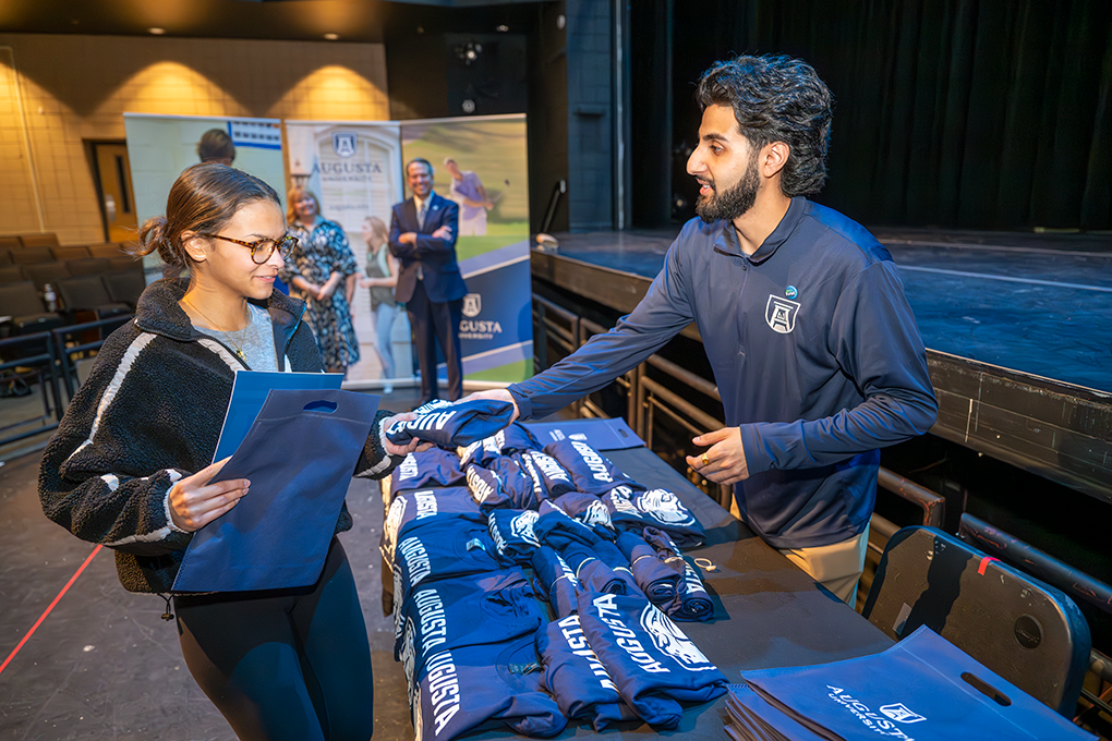 A high school student gets a free t-shirt from a university student.