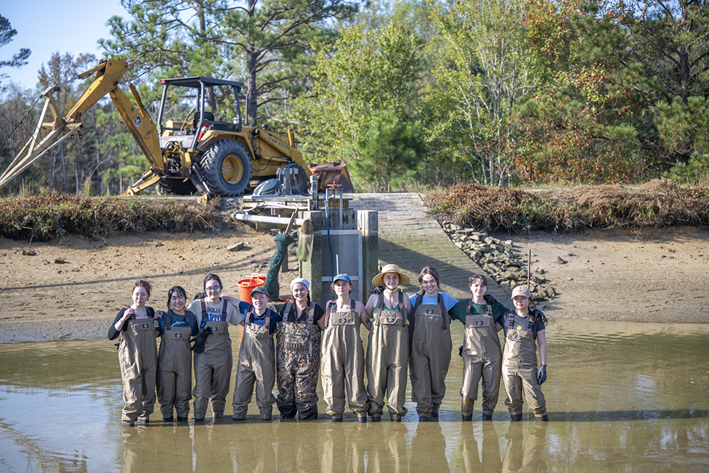 Women standing in a drained pond after moving fish to a tank