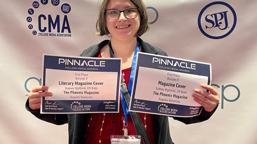 A college-aged woman holding up two paper certificates