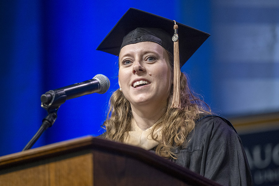 Woman in a graduation cap and gown stands at a podium