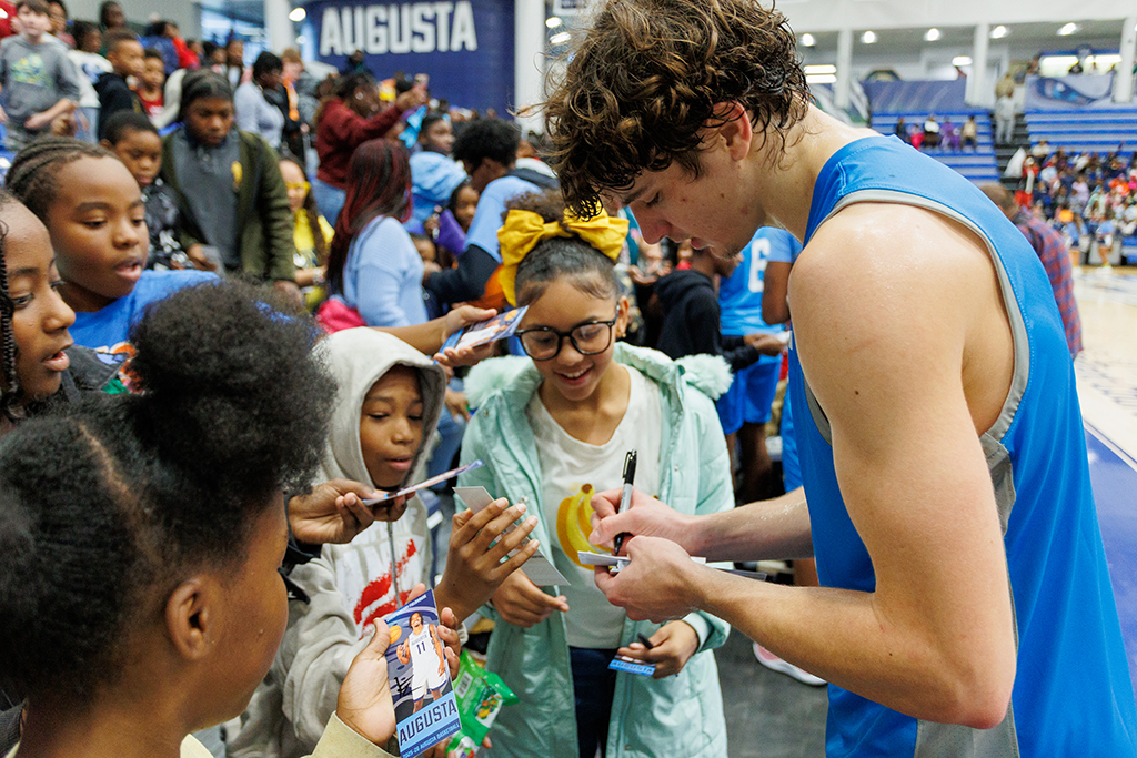 A basketball player signing autographs for boys and girls