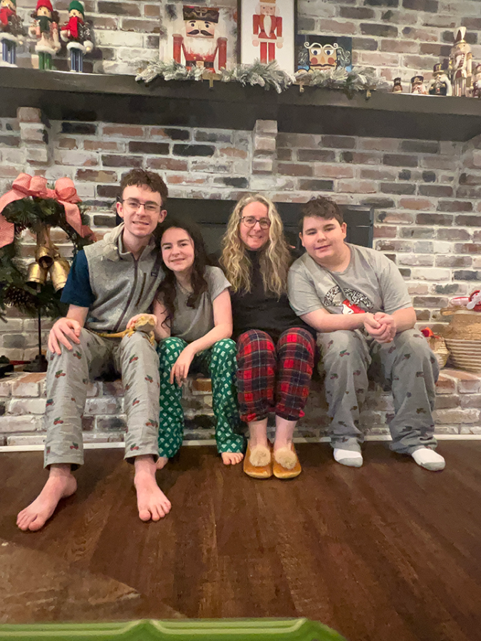 A woman sits on a brick fireplace with her arms around three children, a girl and two boys.