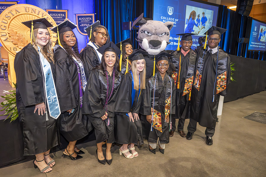 group of females in graduation caps and gowns with a cat mascot. 