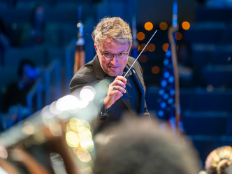 Man in black tie attire holds a conductor's baton.