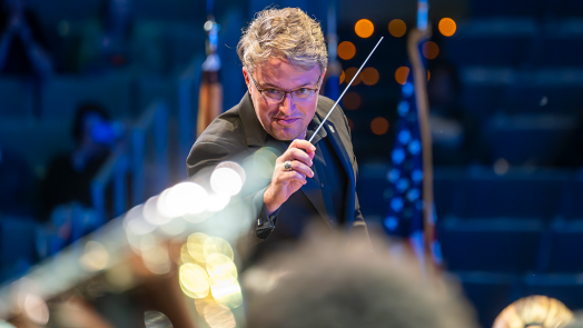 Man in black tie attire holds a conductor's baton.