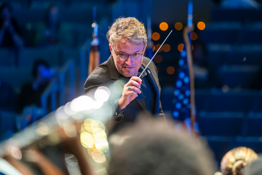 Man in black tie attire holds a conductor's baton.