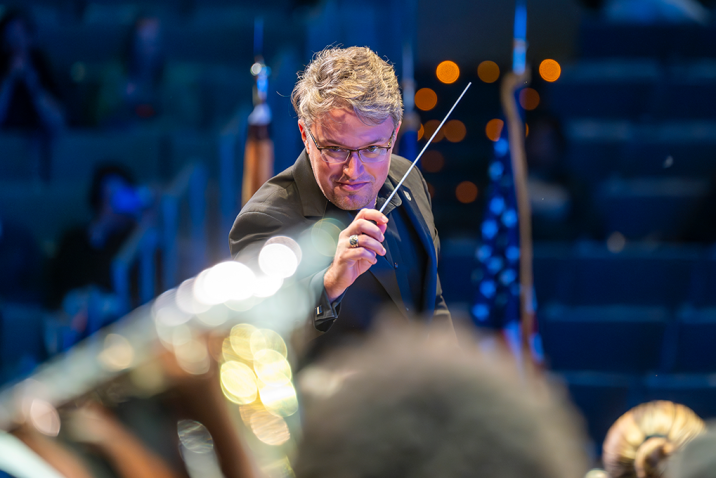 Man in black tie attire holds a conductor's baton.