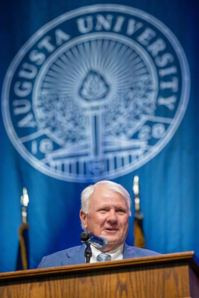 man in a blue suit speaks at a podium.