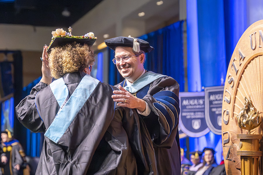 Man in a graduation cap and gown congratulates a student. 