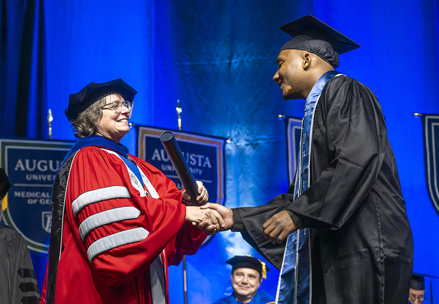 female in a graduation cap and gown smiles at a male student in a graduation cap and gown. 