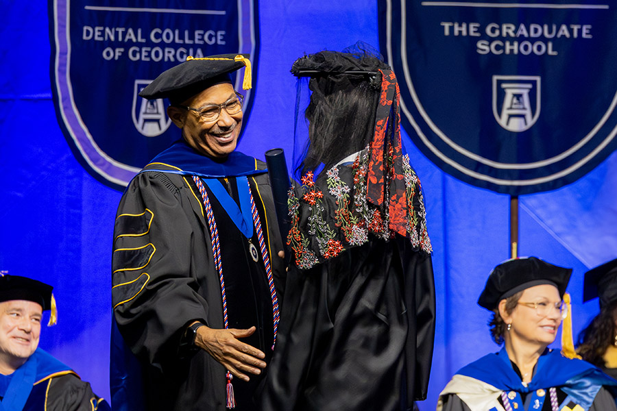 man in a graduation cap and gown smiles at another person in a graduation cap and gown. 